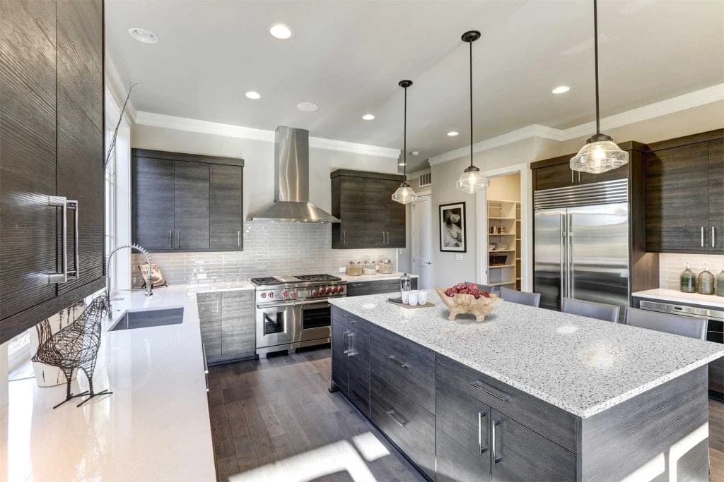 Speckled quartz island and gray cabinetry with stainless appliances — cabinet design from H&E's Houston showroom collection